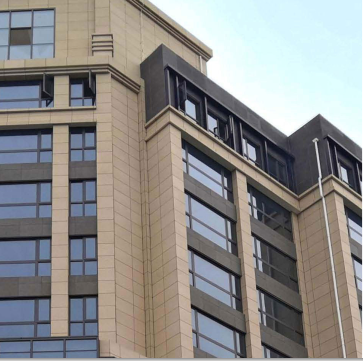 Close-up of a modern building's corner with beige and gray facade under a clear sky.